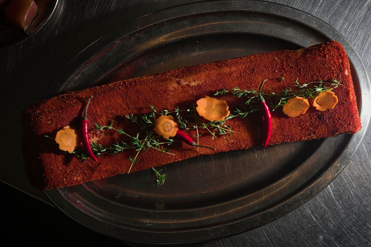 Seasoned meat coated in a spice rub with fresh herbs and pepper, the kind of dry rub application that sets up brisket bark