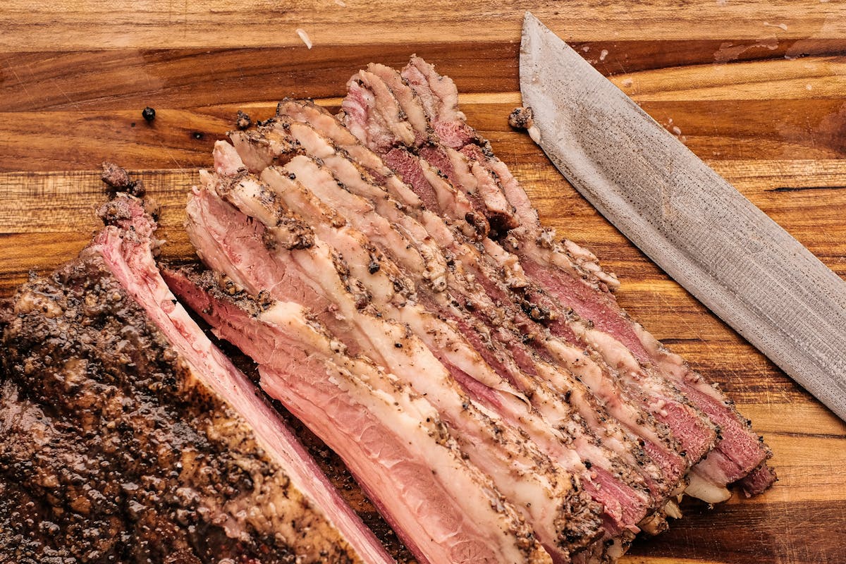 A rested and sliced brisket on a wooden cutting board, the tender payoff after a long faux cambro cooler hold