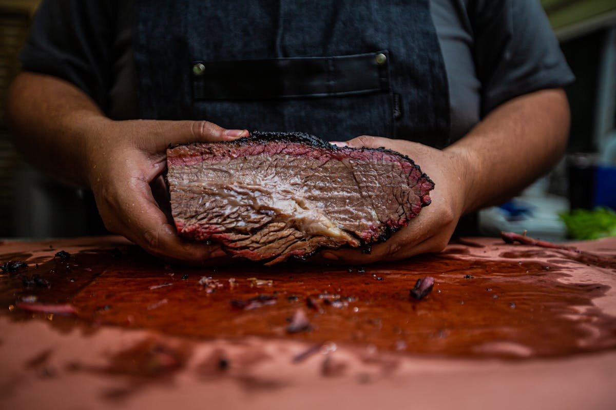 Chef holding a finished smoked brisket with dark bark, the kind of result that only comes after pushing through the stall